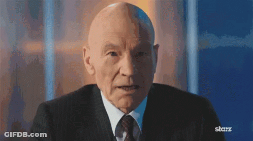 Bald Man In Suit And Tie Sitting In Front Of Blue Wall GIF