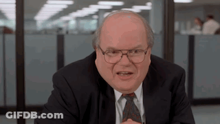 Bald Man In Suit, Tie, And Glasses At Desk GIF