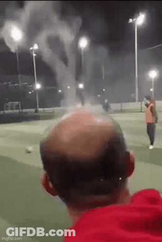 Bald Man Watching Fireworks On Soccer Field At Night GIF