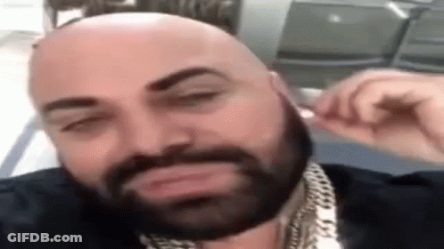 Bald Man With Beard And Chains Adjusting Earbuds GIF