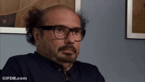 Bald Man With Beard And Glasses Sitting In Front Of Picture GIF