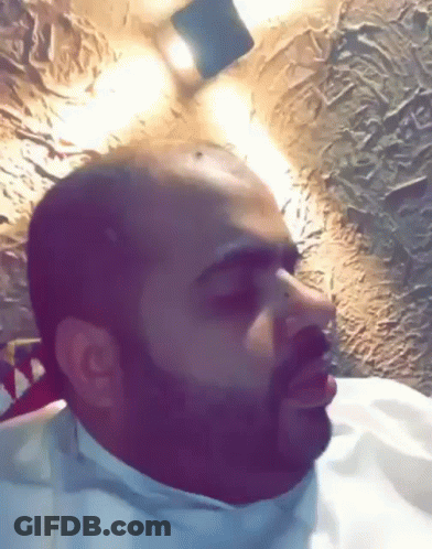 Bald Man With Beard Sitting In Front Of Lit Wall GIF