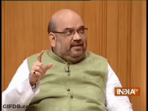 Bald Man With Glasses And Beard Sitting In Front Of Wooden Wall Talking GIF