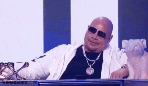 Bald Man With Sunglasses And Necklace Sitting Beside Dog Statue GIF