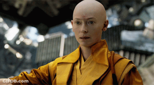 Bald Woman With Cross On Forehead In Yellow Robe GIF