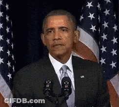 Barack Obama Is Giving A Speech In Front Of A Microphone In Front Of An American Flag . GIF