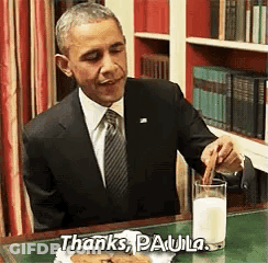 Barack Obama Is Sitting At A Desk With A Glass Of Milk And A Piece Of Food . GIF
