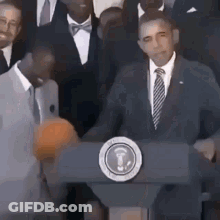 Barack Obama Is Standing At A Podium Giving A Speech While Holding A Basketball . GIF