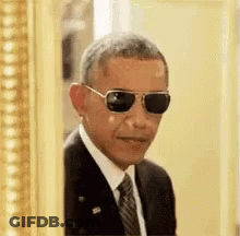 Barack Obama Is Wearing Sunglasses And A Suit And Tie While Peeking Out Of A Picture Frame . GIF