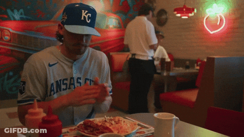 Baseball Player In KC Hat Sitting At Table GIF