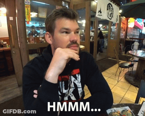 Bearded Man At Table With Hand On Chin Hmmm Sign GIF