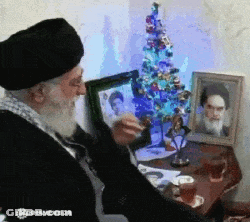 Bearded Man By Christmas Tree Looking At Picture GIF