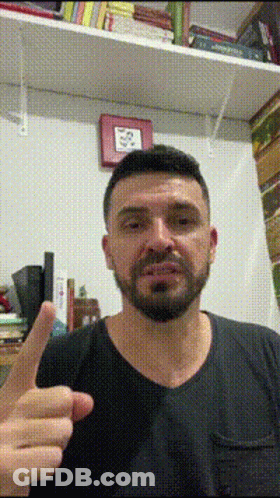 Bearded Man Giving Thumbs Up In Front Of Bookshelf GIF