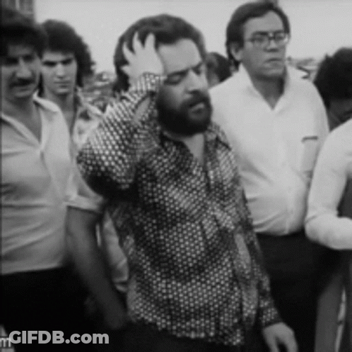 Bearded Man Holding Hand To Head In Crowd GIF