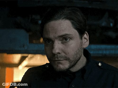 Bearded Man In Black Shirt Looking At Camera In Dark Room GIF