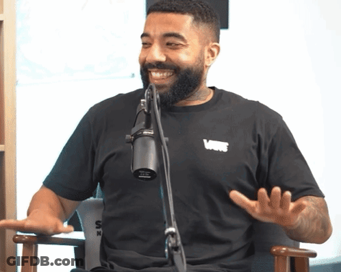 Bearded Man In Black Vans Shirt Talking Into Microphone GIF