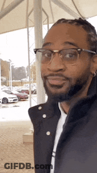 Bearded Man In Glasses And Black Jacket Standing In Parking Lot GIF