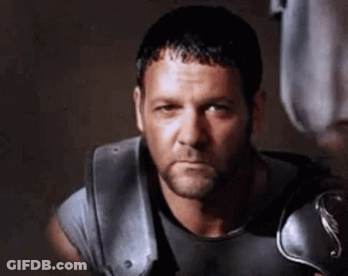 Bearded Man In Gray Shirt And Armor Looking At Camera GIF