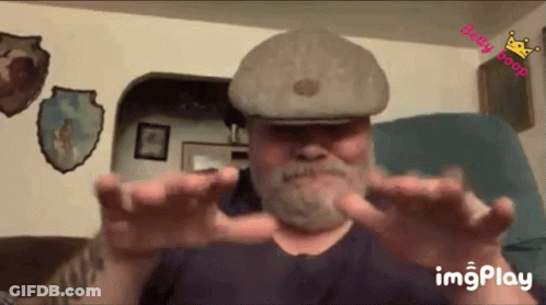 Bearded Man In Hat Sitting With Outstretched Hands GIF