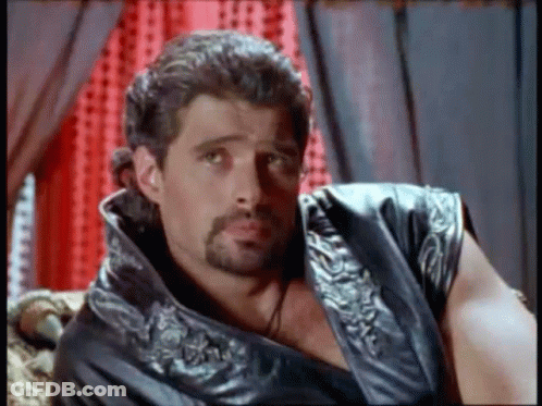 Bearded Man In Leather Vest Sitting On Couch GIF