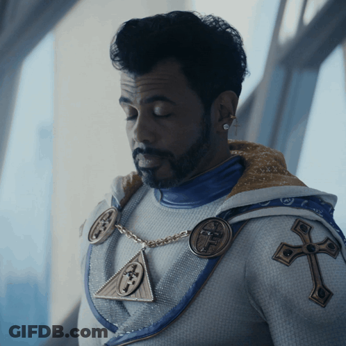 Bearded Man In White And Blue Outfit With Cross GIF