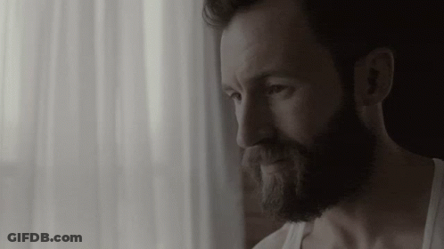 Bearded Man In White Tank Top Looking Out Window GIF