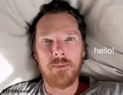 Bearded Man Laying On Bed Saying Hello GIF
