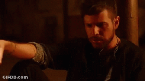 Bearded Man Sitting In Dark Room Holding Hand Out GIF