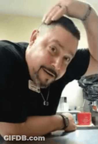 Bearded Man Sitting With Hand On Head Making Funny Face GIF