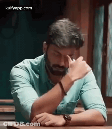 Bearded Man Sitting With Hands On Forehead GIF