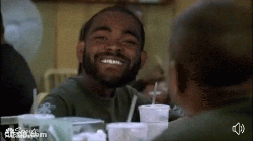 Bearded Man Smiling At Another At Table With Drinks GIF