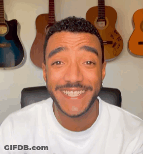 Bearded Man Smiling In Front Of Guitar Wall GIF