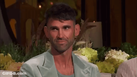 Bearded Man Smiling On Couch With Flowers GIF