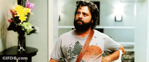 Bearded Man Standing In Front Of Vase Of Flowers GIF