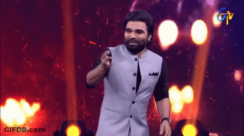 Bearded Man Standing On Stage In Front Of TV Logo GIF