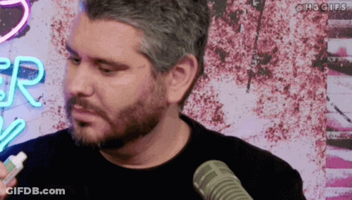 Bearded Man Talking Into Microphone In Front Of Neon R Sign GIF