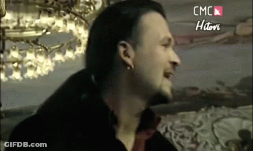 Bearded Man With Earrings Smiling In Front Of Chandelier GIF