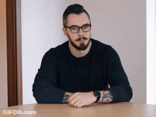 Bearded Man With Glasses Arms Crossed At Table GIF