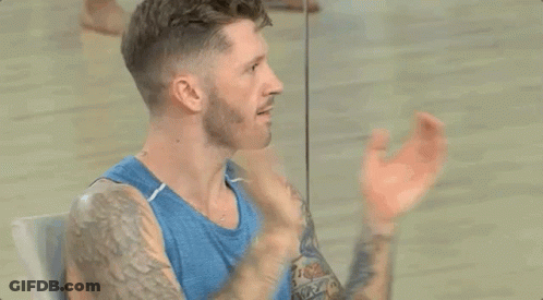 Bearded Man With Tattoos In Blue Tank Top Sitting In Front Of Mirror GIF