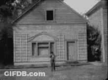 Black And White Man In Front Of Small Wooden House GIF