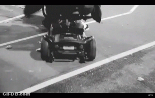 Black And White Person Driving Lawn Mower Down Street GIF