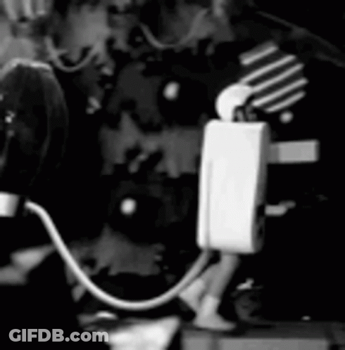 Black And White Person Standing Next To Microphone And Light Bulb GIF