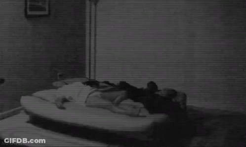 Black And White Photo Of Person Laying On Bed In Dark Room GIF