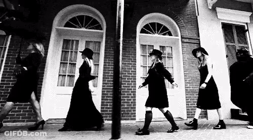 Black And White Photo Of Women Walking Down Sidewalk In Front Of Brick Building GIF