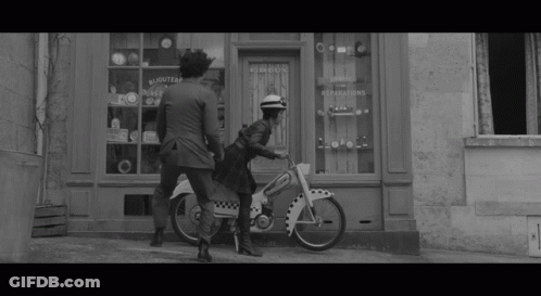 Black And White Woman Riding Motorcycle In Front Of Bijoutier Store GIF