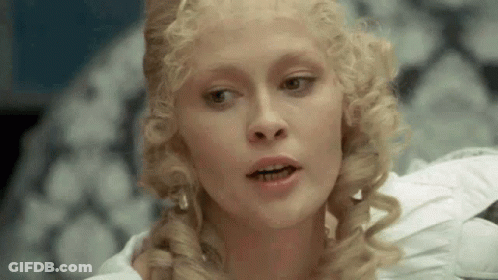 Blonde Curly Hair Woman In White Dress Sitting On Couch GIF