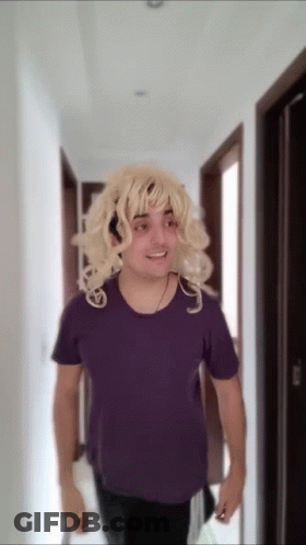 Blonde Wig Man In Purple Shirt Walking Down Hallway GIF