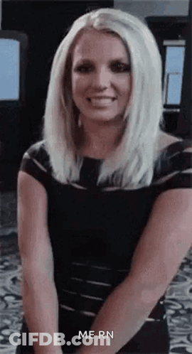 Blonde Woman In Black Dress Smiling With Hands Behind Back GIF