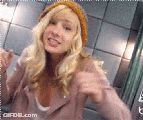 Blonde Woman In Pink Jacket And Yellow Beanie Pointing GIF