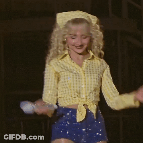 Blonde Woman In Yellow Shirt And Blue Shorts Holding Microphone GIF